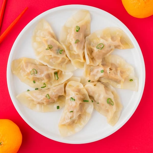 A white plate of Ying Li Restaurant's steamed dumplings, garnished with green onions, on a red background.