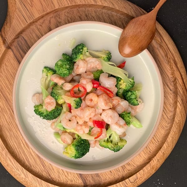 Shrimp and broccoli stir-fry with red chili slices on a light plate, served on a wooden tray.
