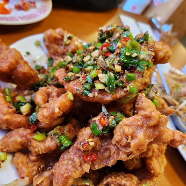 Close-up of crispy fried Chinese chicken pieces topped with chopped green onions and red chilies.